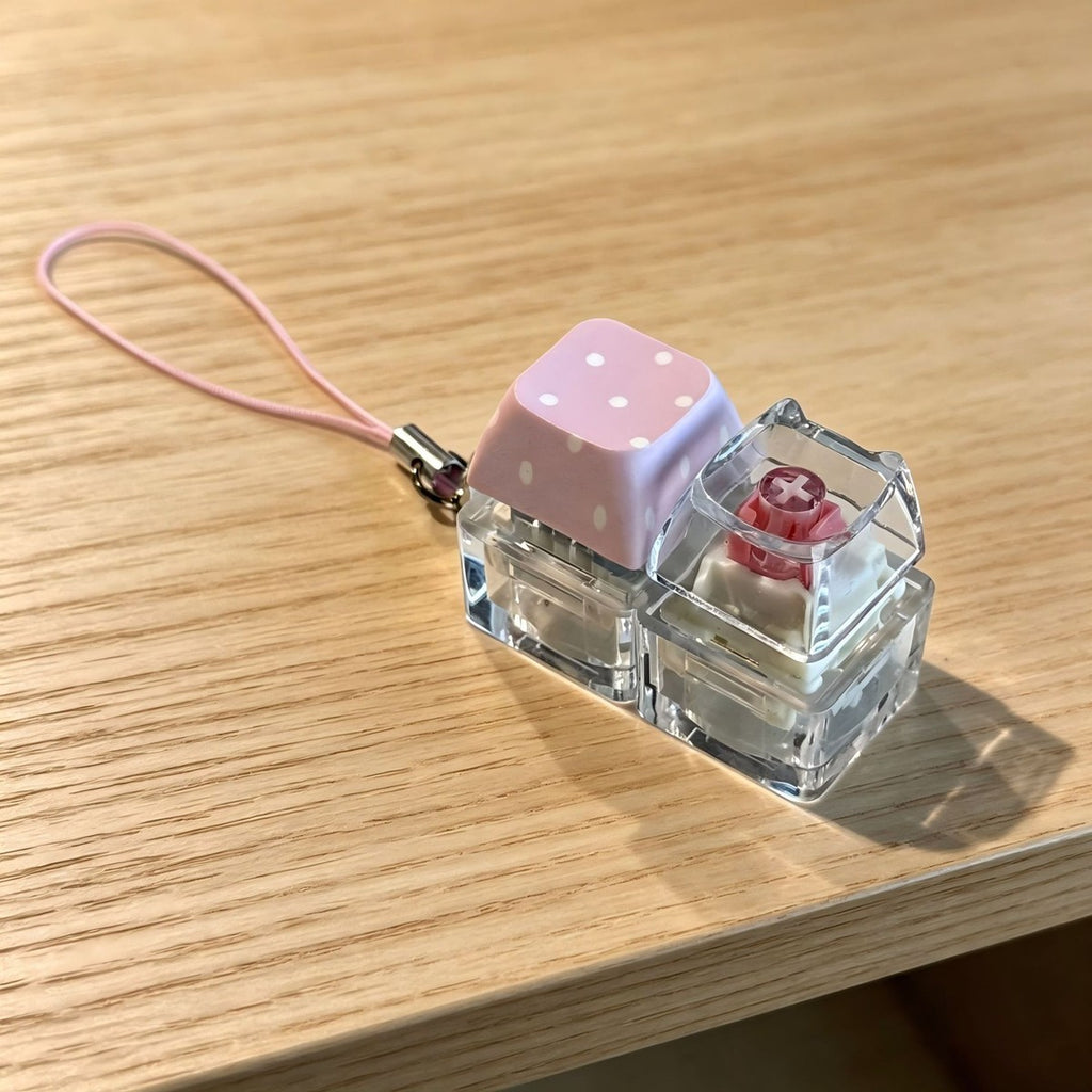 Pink polka-dot cat-head 2-key keycap clicker keychain on a wooden table